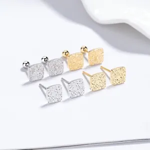 Macro detail of square textured silver stud earrings in gold and silver metal finishes