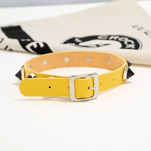 Close-up of a yellow punk leather collar with black cone spikes and silver buckle detail