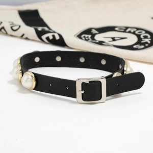 Dettaglio di un choker in pelle nera con grandi perle bianche e castoni dorati