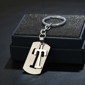 Macro detail of silver rectangular keychain with cutout letter T on brushed metal surface