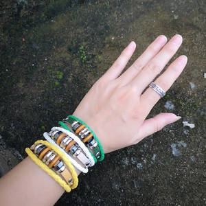 Three-piece braided leather bracelets in green white and yellow with beads on mossy rock