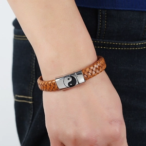 Braided brown leather bracelet with Yin-Yang symbol metal clasp worn on denim background