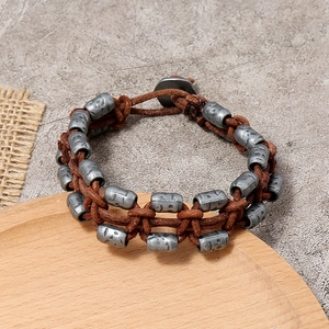 Retro braided brown leather bracelet for men featuring engraved metal beads on rustic background
