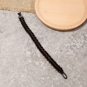 Bracelet tressé à la main en cuir marron foncé avec fermoir anneau sur un plateau en bois