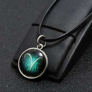 Detailed close-up of Aries zodiac sign pendant with green nebula glass on black leather