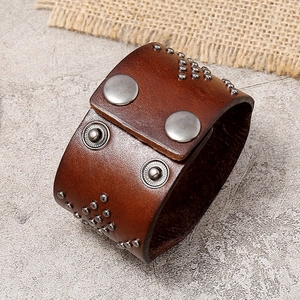 Retro punk style wide brown leather cuff bracelet with silver studs on stone background