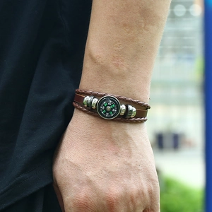 Close-up of a men's multilayer braided leather bracelet with an embedded compass charm