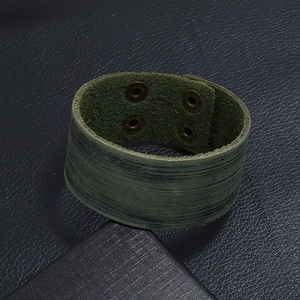 Macro-opname van donkergroene leren armband met bronzen drukknopen en geborstelde textuur