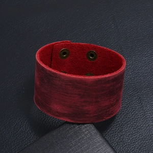 Détail d'un bracelet manchette large en cuir rouge vieilli avec boutons-pression bronze