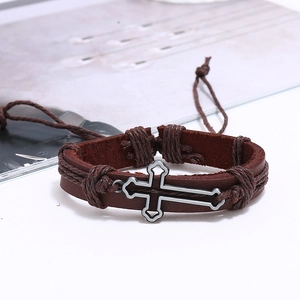 Macro detail of vintage braided leather bracelet set with a metallic cross charm pendant