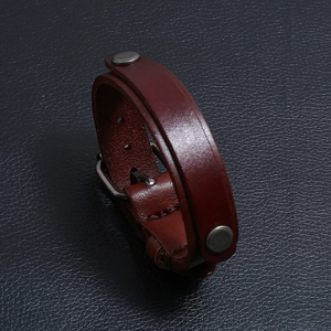Détail d'un bracelet en cuir rouge-brun avec clous en métal et boucle de réglage
