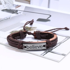 Détail d'un bracelet multicouche en cuir avec plaque en métal gravée du mot 'Believe'