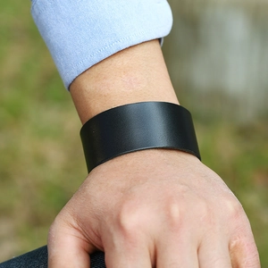 Minimalistische zwarte brede leren herenarmband om de pols gedragen met een blauw shirt