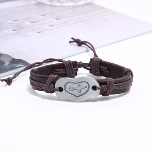 Close-up of vintage brown leather bracelet with silver heart cross metal plate and braided cord