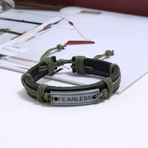 Detail of vintage black leather bracelet with olive cord and FEARLESS engraved metal plate