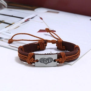 Detail of vintage braided leather bracelet with engraved metal LOVE plate and hearts