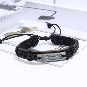 Détail d'un bracelet vintage en cuir tressé avec plaque métallique gravée croix