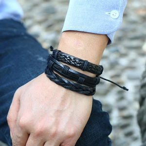 Close-up of men's layered black leather woven bracelets worn in a casual outdoor setting