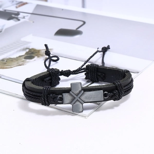 Détail d'un bracelet vintage en cuir noir avec croix métallique et cordon tressé