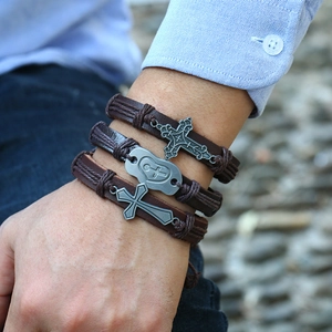 Detail of vintage braided leather bracelet set with metallic cross pendants on male wrist