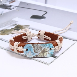 Detail of vintage braided leather bracelet with butterfly print and peace sign charm