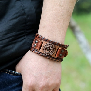 Gros plan sur bracelet en cuir tressé marron avec symbole Om et plaque en nœud celtique