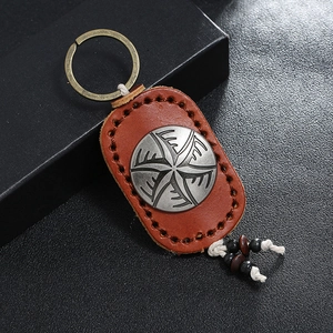 Vintage handmade brown leather keychain with metal emblem and bead tassels on black surface