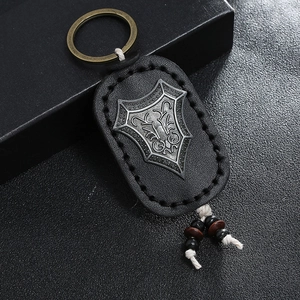 Retro handmade leather keychain with shield emblem and beaded detail on dark background