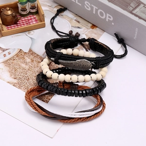 Dettaglio di bracciali in pelle intrecciata vintage con ali metalliche e perline in legno