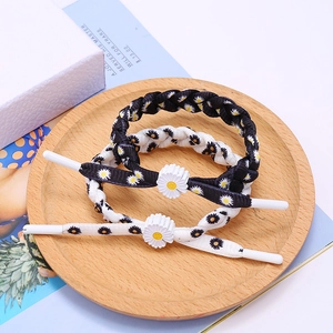 Braided daisy bracelets in black and white colors, displayed on a wooden tray