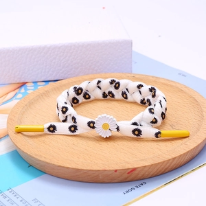 Close-up of woven daisy bracelet with white petals and yellow accents on wooden tray