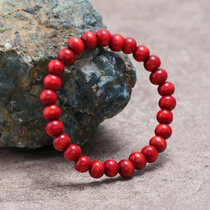 Pulsera minimalista de cuentas de madera roja sobre piedra y fondo gris mate