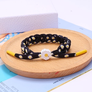 Macro view of woven shoelace bracelet with daisy print and white 3D flower pendant