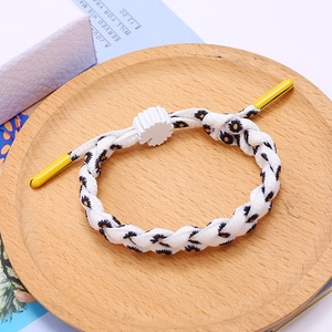 Braided daisy bracelet in white with yellow flower patterns on a wooden tray
