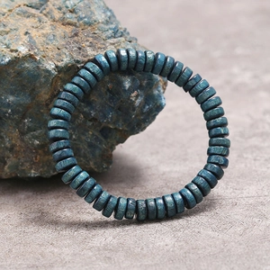 Primer plano de pulsera con cuentas cilíndricas azul mate sobre una piedra natural ruda