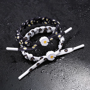 Detail of woven shoelace-style daisy bracelets in black and white with adjustable charms