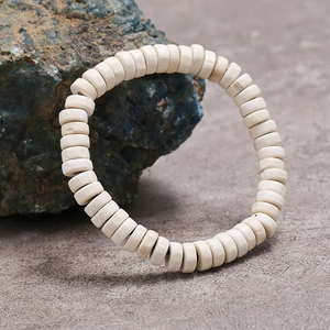 Vista macro de cuentas Heishi de madera blanca en pulsera elástica sobre piedra