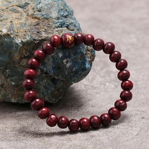 Primer plano de pulsera de cuentas de madera roja con símbolo de Buda dorado en roca