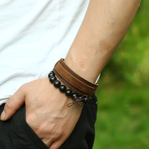 Men's vintage brown leather cuff and black wooden bead bracelet set worn outdoors