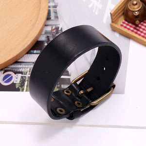 Detail of black leather cuff bracelet with adjustable bronze buckle on a rustic background