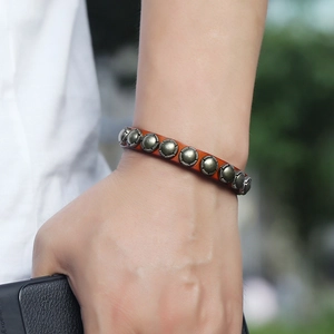 Retro punk brown leather bracelet with carved bronze rivets worn on a wrist in nature