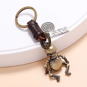 Vintage bronze skeleton keychain with woven leather and engraved metal charms on white stand
