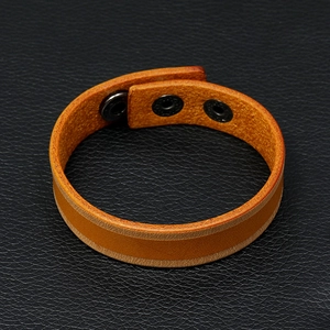 Detail van de bruine leren armband met drie verstelbare metalen drukknopen op zwarte achtergrond