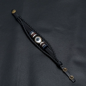 Braided black leather bracelet with blue evil eye bead and metallic accents