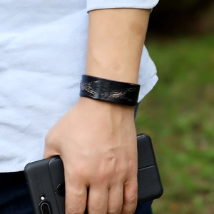 Retro black leather wristband with distressed gold texture worn on wrist in outdoor setting