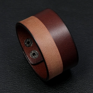 Macro shot of two-tone brown leather cuff with dual metal snaps on black textured base