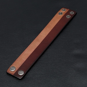 Macro detail of two-tone brown leather wristband featuring adjustable silver metal snap buttons