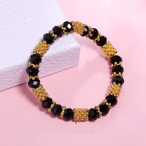 Close-up of black faceted crystal beads and gold engraved cylinders on elastic bracelet