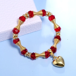 Detail of red crystal beaded bracelet with gold heart pendant on white leather background