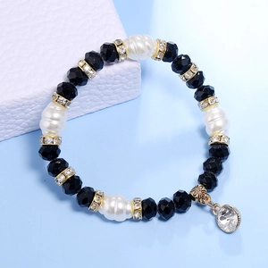 Detalle de pulsera con cuentas facetadas negras, perlas grandes y dijes dorados